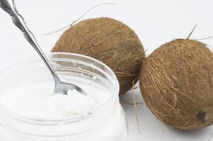 Coconut oil in a container with spoon and two coconuts.
