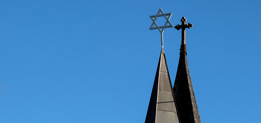 Perspective of church and synagogue spires atopped with a cross and Star of David.  The two spires appear to be overlapping in a clear sky.